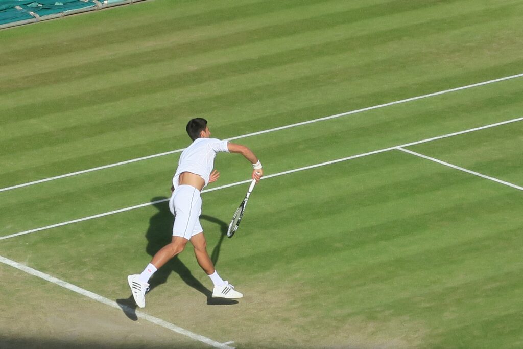 Novak Djokovic playing tennis on a grass court. He is one of the most common answers to who will win Wimbledon this year. 